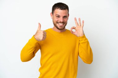 Beyaz arka planda izole edilmiş genç Brezilyalı adam işaret ve baş parmak hareketi gösteriyor.