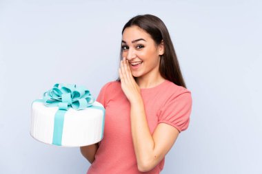 Pasta şefi elinde büyük bir pasta tutarken mavi arka planda bir şeyler fısıldıyor.