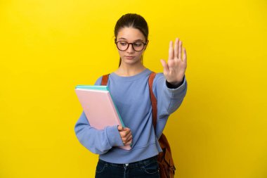 İzole edilmiş sarı arka planda öğrenci bir kadın dur hareketi yapıyor ve hayal kırıklığına uğruyor.