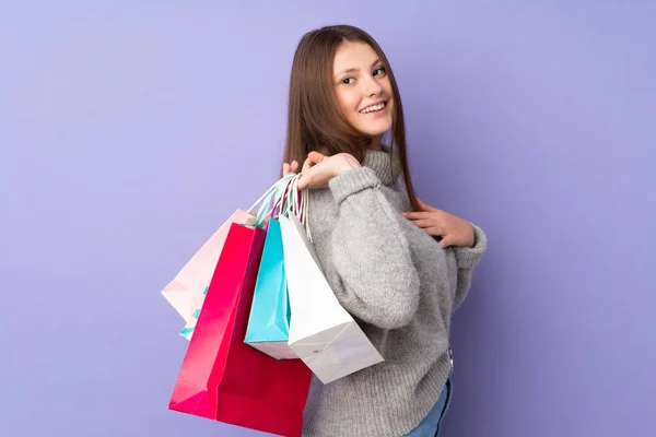 ティーンCaucasian女の子隔離上の紫背景保持ショッピングバッグと笑顔 — ストック写真