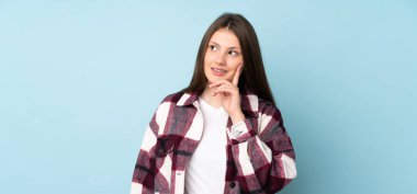 Kafkasyalı genç bir kız mavi arka planda izole edilmiş bir şekilde yukarı bakarken bir fikir düşünüyor.