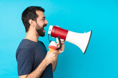 Kornet dondurmalı genç adam izole edilmiş mavi arka planda megafondan bağırıyor.