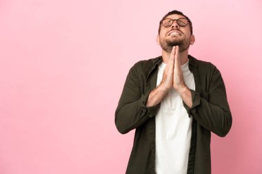 Pembe arka planda izole edilmiş genç Brezilyalı adam avuç içlerini bir arada tutuyor. İnsan bir şey ister.