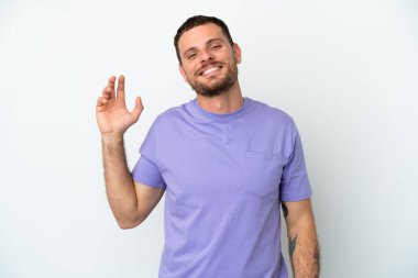Genç Brezilyalı adam beyaz arka planda izole edilmiş, mutlu bir ifadeyle selamlıyor.