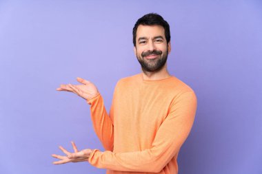 İzole edilmiş mor arka planda beyaz, yakışıklı bir adam. Gelmesi için ellerini yana uzatıyor.