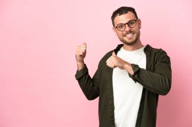 Pembe arka planda izole edilmiş genç Brezilyalı bir adam bir ürün sunmak için kenarı işaret ediyor.