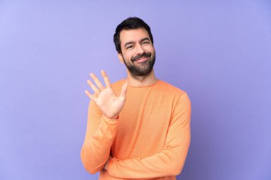 İzole edilmiş mor arka planda beyaz yakışıklı adam parmaklarıyla beşi sayıyor.