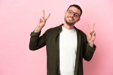 Pembe arka planda izole edilmiş genç Brezilyalı iki eliyle zafer işareti gösteriyor.