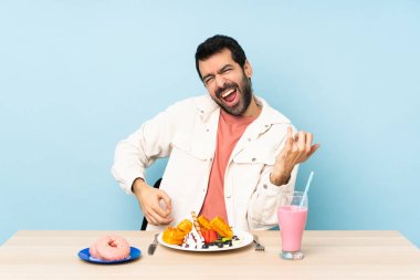 Masadaki adam kahvaltı yapıyor ve milkshake içiyor. Gitar jesti yapıyor.