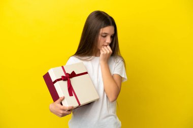 İzole edilmiş sarı arka planda küçük bir kızın elinde bir hediye var. Şüpheleri var.