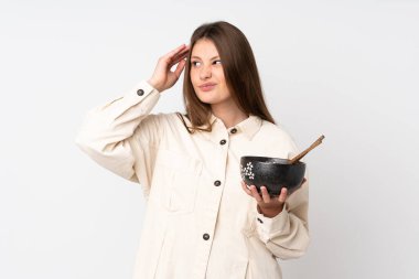 Beyaz arka planda izole olmuş beyaz bir kız. Kafası karışmış bir halde elinde yemek çubuklarıyla elinde bir kase erişte tutarken...