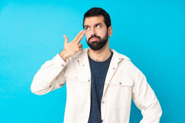 Beyaz kadife ceketli genç, mavi arka planda intihar jesti yapmada sorun yaşayan yakışıklı bir adam.