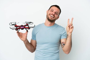 Beyaz arka planda izole edilmiş bir İHA tutan genç Brezilyalı adam gülümsüyor ve zafer işareti gösteriyor.