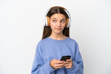 Küçük kız izole edilmiş beyaz arka planda müzik dinliyor ve düşünüyor.