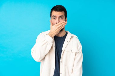 Beyaz kadife ceketli genç yakışıklı adam izole edilmiş mavi arka planda elleri ve ağzı kapalı.