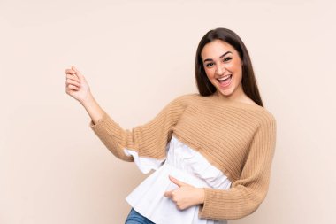 Beyaz tenli genç bir kadın bej arka planda izole edilmiş gitar hareketi yapıyor.