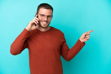Mavi arka planda izole edilmiş cep telefonu kullanan genç Brezilyalı bir adam.