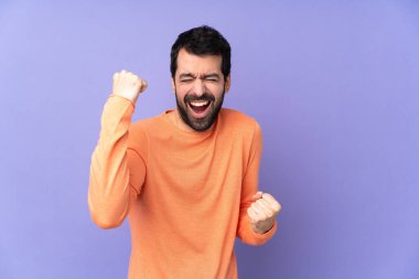 İzole edilmiş mor arka planda beyaz yakışıklı bir adam zaferi kutluyor.