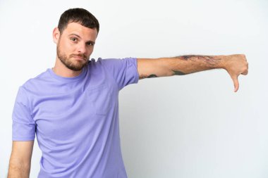 Beyaz arka planda izole edilmiş genç Brezilyalı adam olumsuz ifadeyle baş parmağını aşağı gösteriyor.