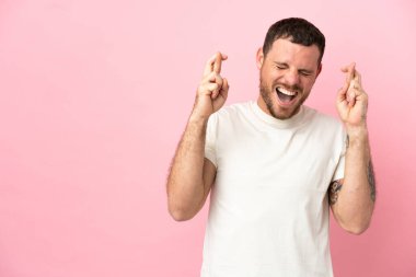 Pembe arka planda izole edilmiş genç Brezilyalı adam şans diliyor.