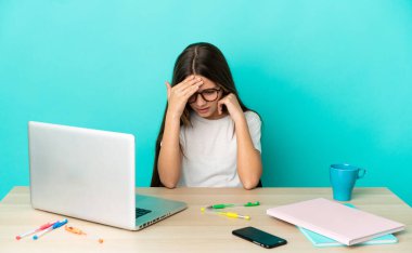 Masada dizüstü bilgisayarı olan küçük bir kız izole edilmiş mavi arka plan ve baş ağrısı.