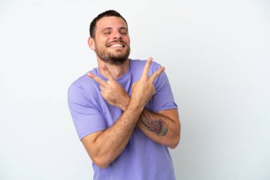 Beyaz arka planda izole edilmiş genç Brezilyalı adam gülümsüyor ve zafer işareti gösteriyor