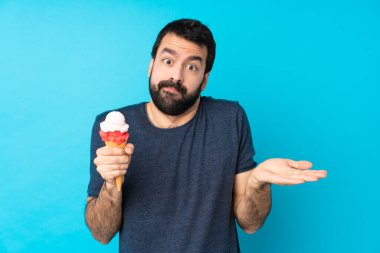 Kornet dondurması ile izole edilmiş mavi arka planı olan genç adam şüpheli hareketler yapıyor.