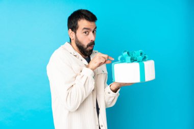 Büyük pastası olan genç ve yakışıklı bir adam izole edilmiş mavi arka planda