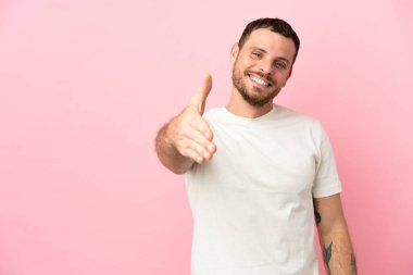 Pembe arka planda izole edilmiş genç Brezilyalı adam iyi bir anlaşma için el sıkışıyor.