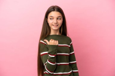 İzole edilmiş pembe arka planda küçük bir kız bir ürün sunmak için kenarı işaret ediyor.