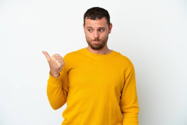 Genç Brezilyalı adam beyaz arka planda izole edilmiş mutsuz ve kenarı işaret ediyor.