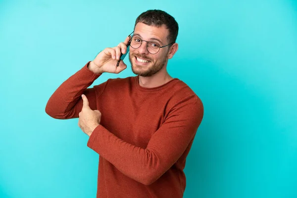 Mladý Brazilský Muž Pomocí Mobilního Telefonu Izolované Modrém Pozadí Ukazuje — Stock fotografie