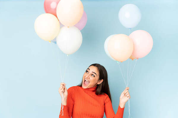 Young woman catching many balloons isolated on blue background