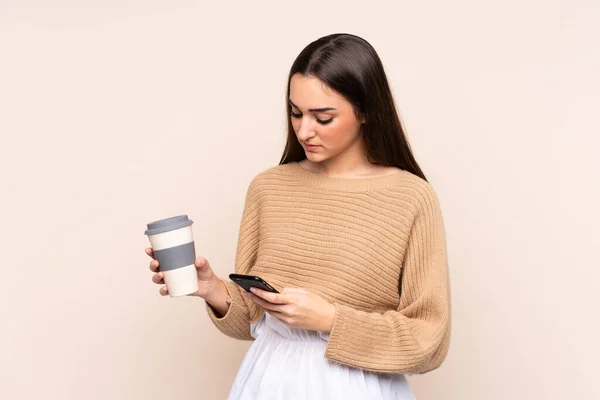 Jovem Caucasiana Isolada Fundo Bege Segurando Café Para Levar Celular — Fotografia de Stock