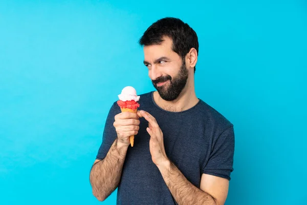 Young man with a cornet ice cream over isolated blue background scheming something