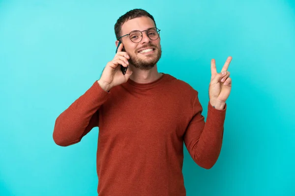 Mladý Brazilský Muž Pomocí Mobilního Telefonu Izolované Modrém Pozadí Úsměvem — Stock fotografie
