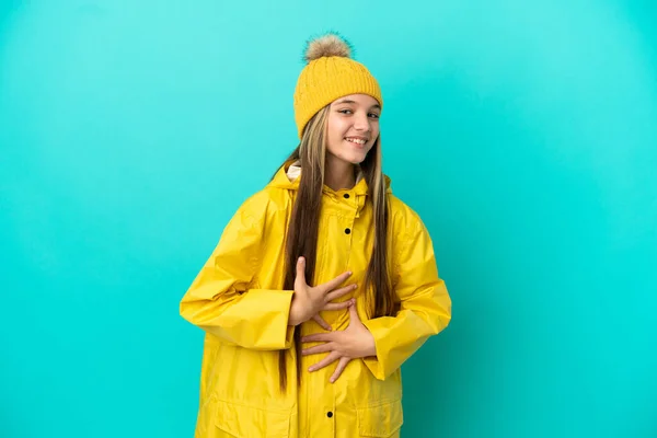 穿着防雨外套的小女孩在孤零零的蓝色背景上笑了很多 — 图库照片