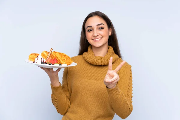 Jonge Kaukasische Vrouw Houden Wafels Geïsoleerd Blauwe Achtergrond Glimlachen Tonen — Stockfoto