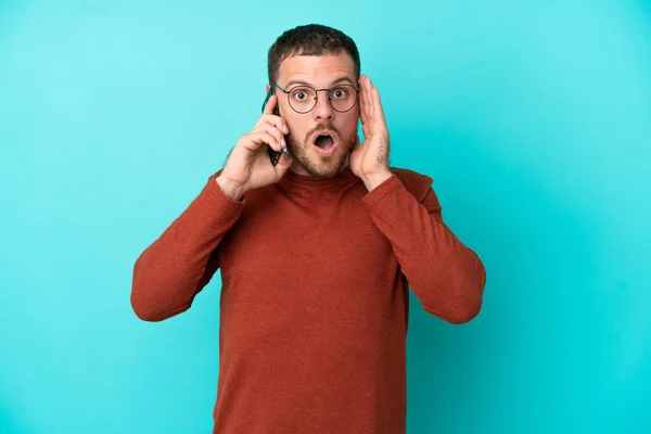 Young Brazilian Man Using Mobile Phone Isolated Blue Background Surprise — Stock Photo, Image