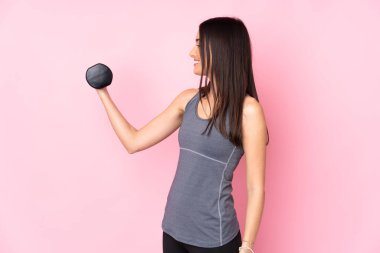 Pembe arka planda halter kaldıran genç kadın mutlu bir ifadeyle izole edilmiş.