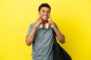 Sarı arka planda izole edilmiş spor çantalı genç Afrikalı Amerikalı mutlu ve hoş bir ifadeyle gülümsüyor.