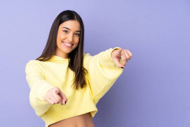 İzole edilmiş arka planda genç beyaz kadın mutlu bir ifadeyle ön tarafı işaret ediyor