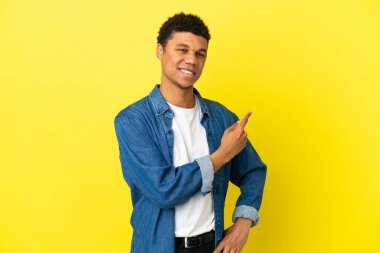 Sarı arka planda izole edilmiş genç Afrikalı Amerikalı bir ürün sunmak için kenarı işaret ediyor.