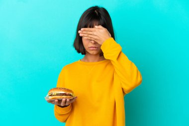 Elinde hamburger tutan genç esmer kadın izole edilmiş arka planda gözlerini elleriyle kapatıyor. Bir şey görmek istemiyorum.