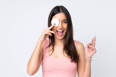 Beyaz arka planda, makyajını silmek ve gülümsemek için pamuklu ped kullanan beyaz bir kadın.