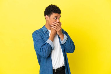 Genç Afrikalı Amerikalı adam sarı arka planda izole edilmiş ağzını kapatıyor ve yan tarafa bakıyor.