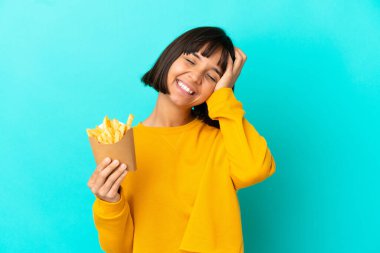 Genç esmer kadın, izole edilmiş mavi arka planda patates kızartması tutuyor ve gülümsüyor.