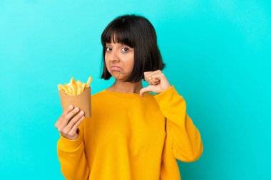 Genç esmer kadın izole edilmiş mavi arka planda kızarmış patates kızartması tutuyor gururlu ve kendini beğenmiş.