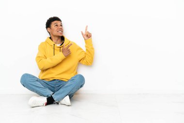 Beyaz arka planda izole bir şekilde yerde oturan genç Afrikalı Amerikalı işaret parmağıyla işaret etmek harika bir fikir.