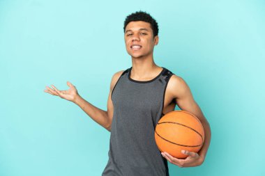 Basketbolcu Afrikalı Amerikalı adam mavi arka planda izole edilmiş. Davet etmek için ellerini yana uzatıyor.